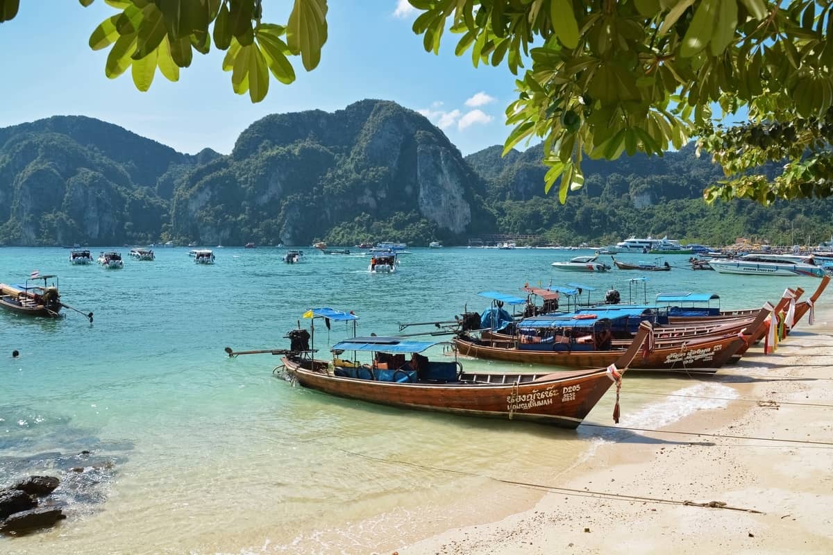 Longtail boat parked at a beach in Thailand with rocky hills at the back