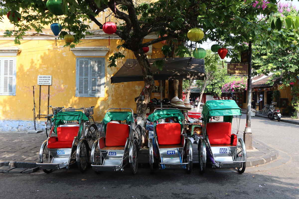 Richshaws parked by a greenery-lined wall.