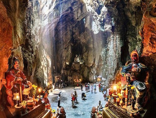 Large cave interior with people and illuminated stalactites.