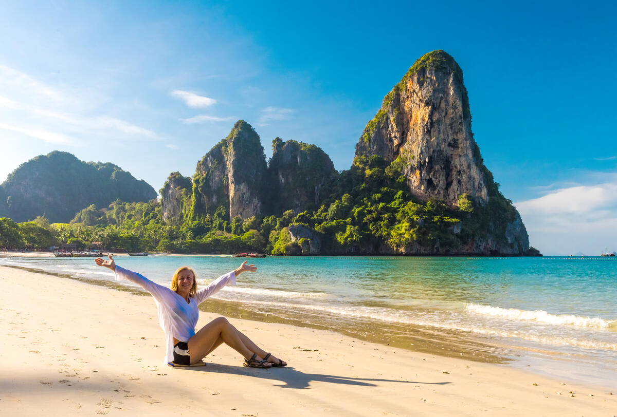 Woman posing for a photo on a beach with a towering rock formation.