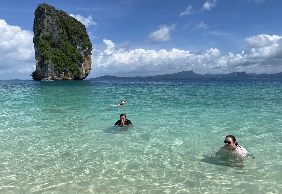 Tourists swimming in turquoise waters near cliffs.