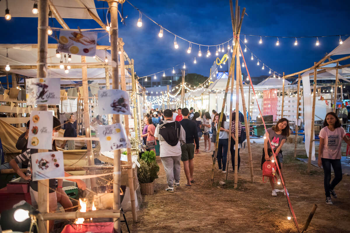 People walking through a night market with tents.